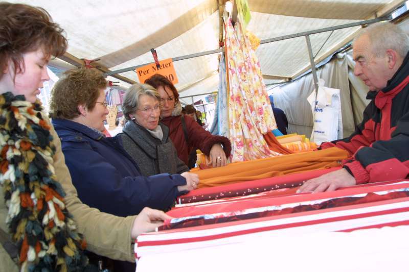 marktkoopman toont stoffen aan klanten in zijn marktkraam